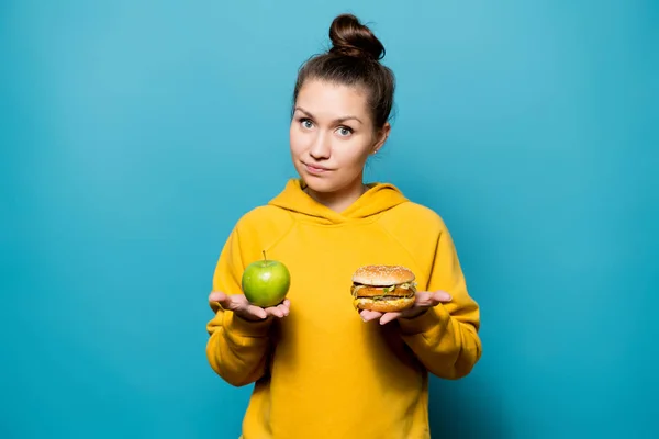 Mooi meisje houdt een appel en een hamburger in haar handpalmen — Stockfoto