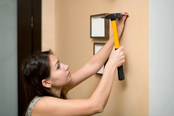 Flicka hamra en spik i väggen för att hänga en fotoram — Stockfoto