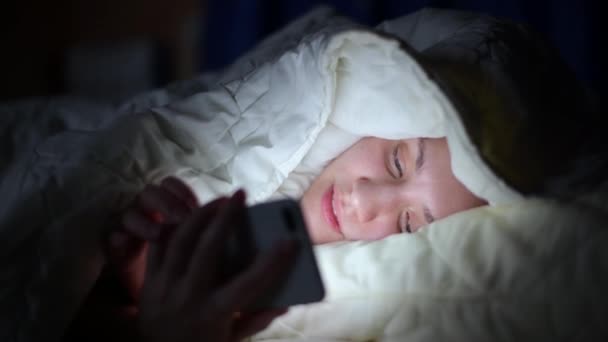 Fille regarde les réseaux sociaux à cause de l'insomnie, couché sous une couverture . — Video