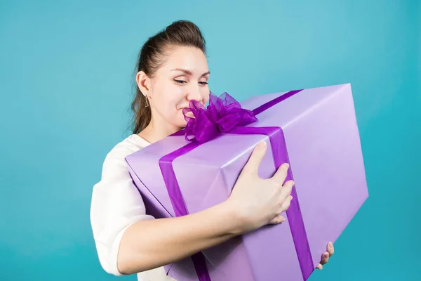 Girl holds a big gift, smiling warmly and looking at it