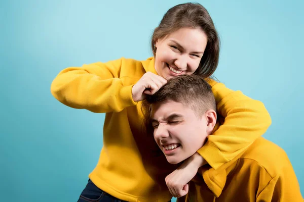 Ältere Schwester scherzt mit kleinem Bruder, blauer Hintergrund — Stockfoto