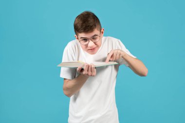 İnek, omuzlarını sıkıyor, bir gözünü kısıyor, bir kitabı işaret ediyor.