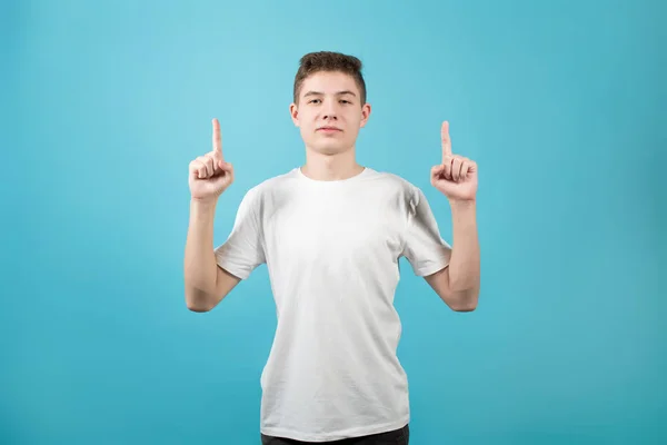 Joven en camiseta blanca señala los dedos índice hacia arriba y sonríe — Foto de Stock