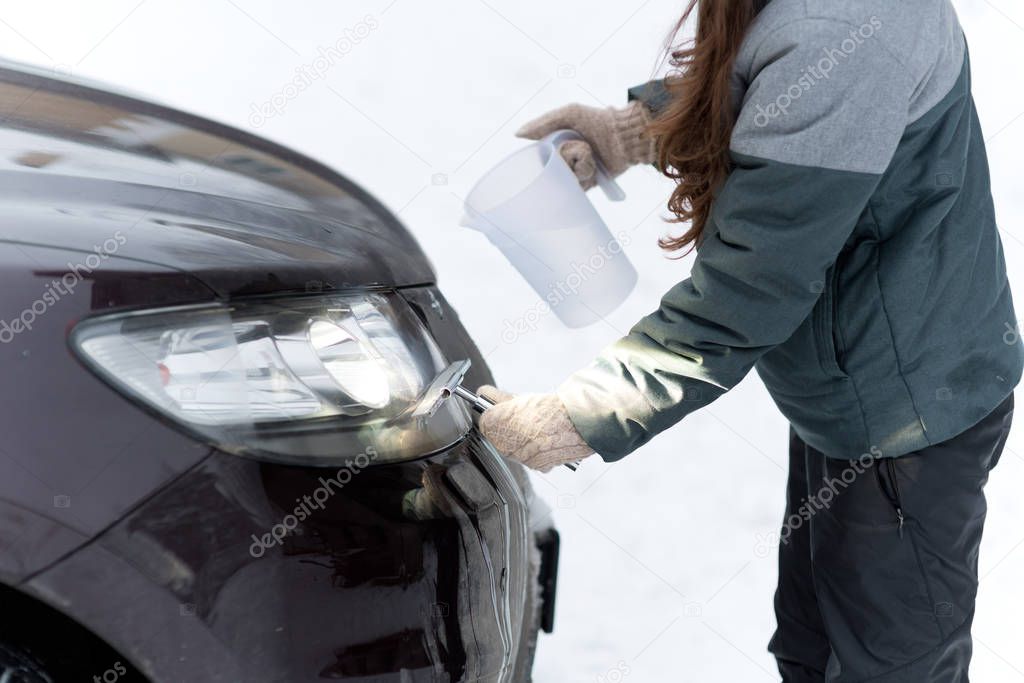 Girl cleans the headlights of a car before the road trip with the help of warm water