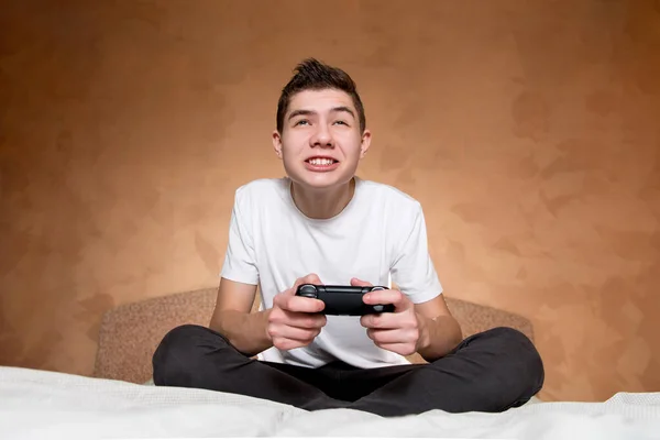 Um menino em uma camiseta branca joga com entusiasmo um jogo de vídeo usando o joystick — Fotografia de Stock