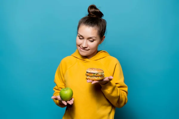 Aardig meisje gaat geven de voorkeur aan een hamburger in plaats van een appel — Stockfoto