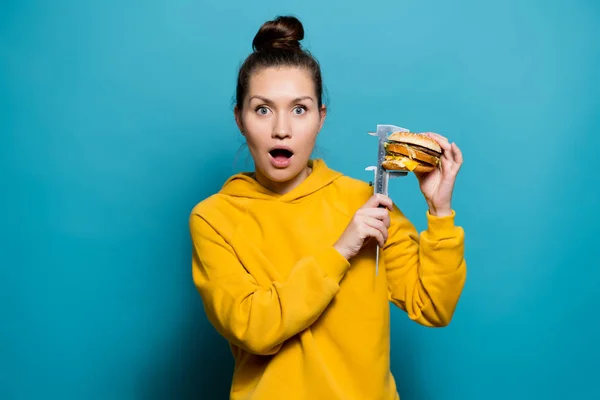 Meisje toont schok door het meten van de hoogte van een hamburger met een schuifmaat — Stockfoto