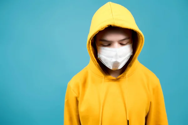 teenager in a yellow sweatshirt on a blue background with a medical bandage on his face