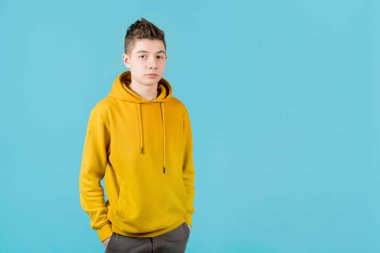 Mavi arka planda sarı kazaklı, ciddi bir genç adam.