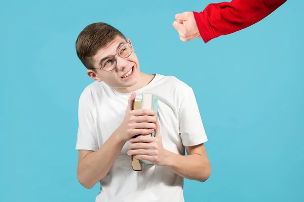 Punho de um valentão em uma camisola vermelha ameaça um nerd com óculos com um livro — Fotografia de Stock