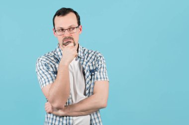 Gözlüklü kıllı bir adam düşünceli bir şekilde uzaklaşıyor, çenesini ovalıyor.