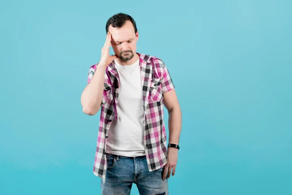 Homem com restolho em uma camisa xadrez segura a mão para a cabeça, representando a dor — Fotografia de Stock