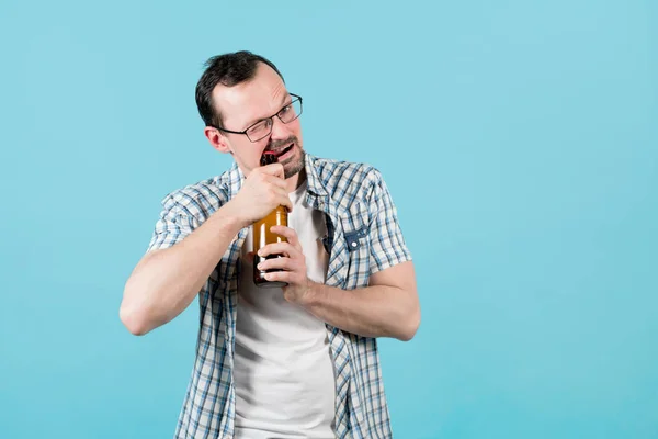 Een man opent een fles bier met zijn tanden en kijkt naar de camera — Stockfoto