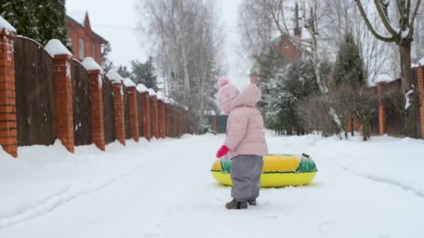 A small child tries to pull an inflatable circle on a rope on a snowy winter day — Stock Video