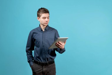 Ciddi görünümlü bir genç, bir eli cebinde tablete bakar..