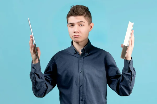 Um adolescente segura um tablet em uma mão e um livro na outra mão . — Fotografia de Stock