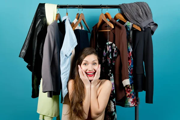 Młoda kobieta na tle różnych ubrań uśmiecha się i trzyma twarz — Zdjęcie stockowe