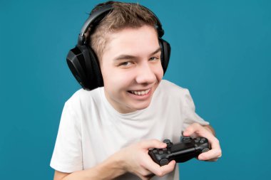 Elinde oyun konsolunun joystick 'iyle kulaklıklı gülümseyen okul çocuğu, yakın plan.