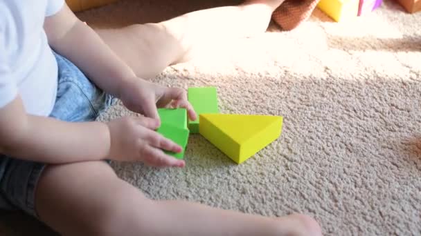 Una niña pequeña se sienta en el suelo y gira dos figuras verdes en sus manos . — Vídeos de Stock