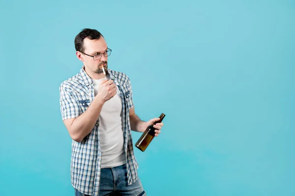 L'homme allume une cigarette, tenant une bouteille de bière, mais quelque chose l'a distrait et il regarde ailleurs — Photo