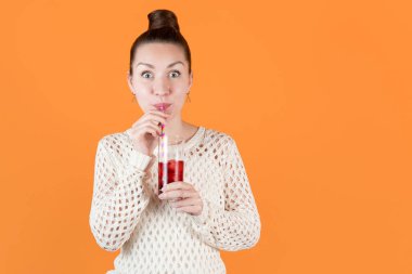 Kız çizgili kamışlardan soğuk kiraz suyu içiyor ve gözlerini açıyor, portakalda izole bir şekilde.