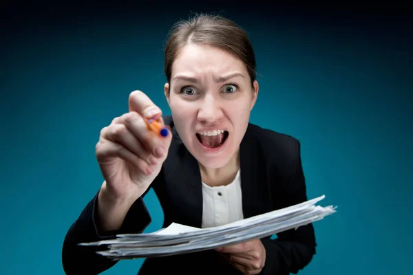 a woman in an office suit with a strict haircut screams into the camera, pokes with a pen and waving documents. Blue background