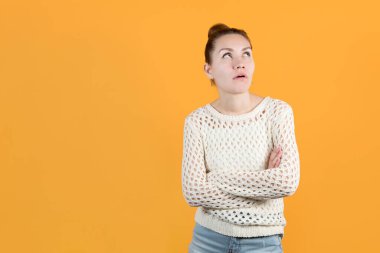 Kız kollarını göğsünün üzerine bağladı ve şüphecilik ve yorgunlukla kafasını kaldırdı. Turuncu sarı arka planda izole edilmiş..