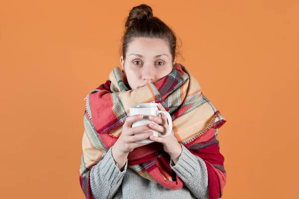 那女孩感冒了 她用温暖的毯子捂住喉咙 手里拿着一杯热饮 在橙色的黄色背景上分离 — 图库照片