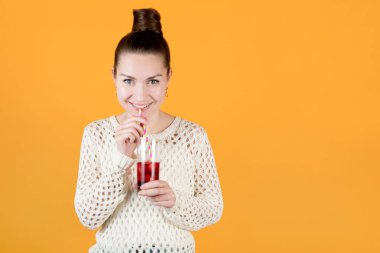 Kız elinde soğuk meyve suyu, çizgili pipet ve gülümsemeyle bir bardak tutuyor. turuncu-sarı üzerinde izole