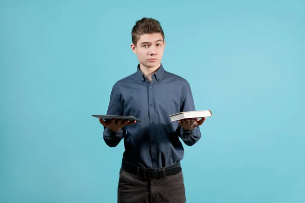 Een tiener in een blauw shirt houdt een tablet en een boek voor zich. — Stockfoto