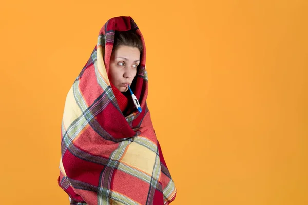 Mädchen hüllt sich in einen karierten Karo und hält ein Thermometer im Mund — Stockfoto