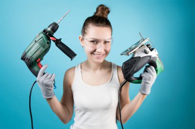 Kurnazca gülümseyen bir kız ve elinde elektrikli aletler - bir yapboz ve matkap. Mavi üzerine izole edilmiş.