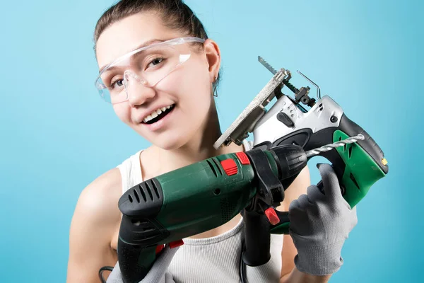 Smiling woman and power tools - electric drill and jigsaw. Close up