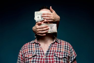 Karanlıktan gelen eller, çalışan bir adamın gözlerini ve ağzını dolarlarla kapatır. Para gözünü kör etmiş.