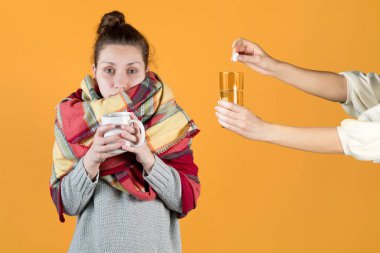 Ekose kumaşa sarılmış hasta bir kız, coşkun bir tablet şeklinde çözünebilir bir antipiretik içmeye davet edilir. Turuncu arka planda izole edilmiş