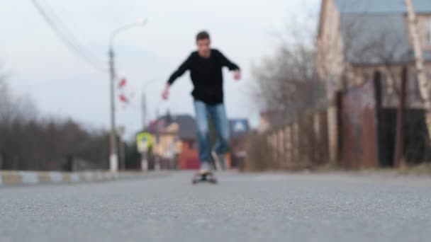 Um adolescente monta em um skate e pára perto da câmera na área de foco . — Vídeo de Stock