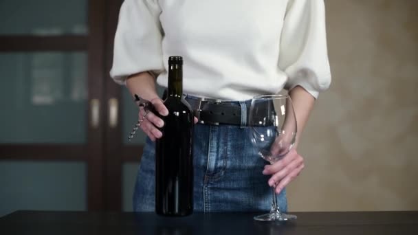 La ragazza viene a tavola con una bottiglia di vino e un bicchiere e inizia ad aprire il vino — Video Stock