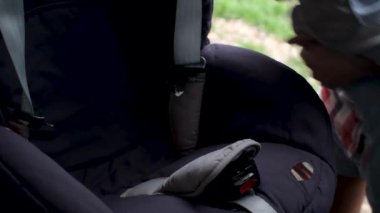 Anne arabanın kapısını açar ve çocuğunu araba koltuğuna bağlar.