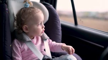 Çocuk koltuğundaki küçük kız araba sürerken pencereden dışarı bakar.