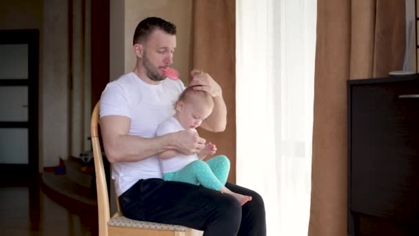 A young father spends time with a little daughter. Dad braids a ponytail — Stock Video
