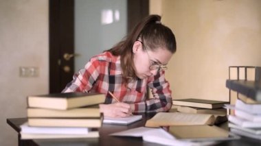 Kız okuyarak ve not alarak sınavlara hazırlanıyor. O bir masada oturuyor.