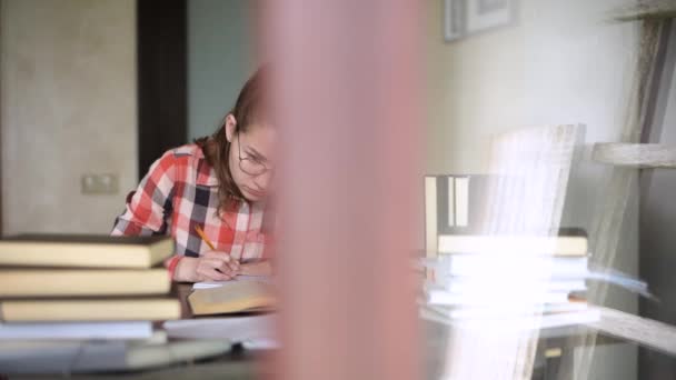 Kamera porusza się za oknem, pokazując dziewczynę, która przygotowuje się do egzaminów — Wideo stockowe