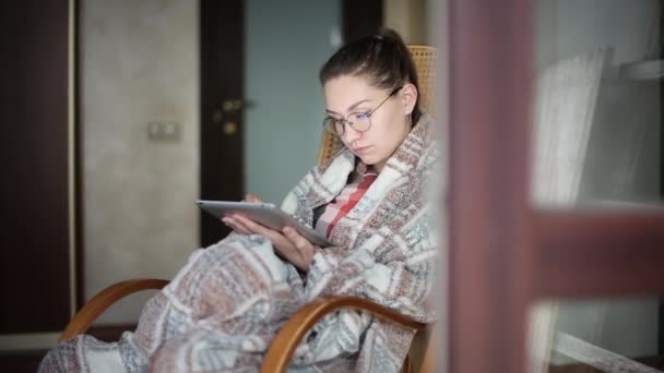 Mädchen im Schaukelstuhl mit Tablet liest E-Book, Nachrichten oder surft im Internet — Stockvideo