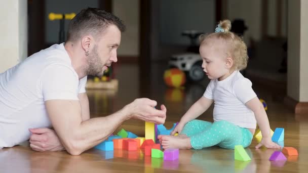 Papa speelt met zijn dochter in gekleurde stukken op de vloer. Vader en kind — Stockvideo