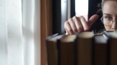 Kamera, kızın bir kitap seçtiği kitap sırası boyunca hareket eder.