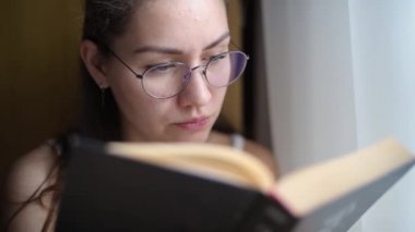 Genç bir kadın kitap okuyor, bir kitabın arkasından bakıyor, yakın plan.