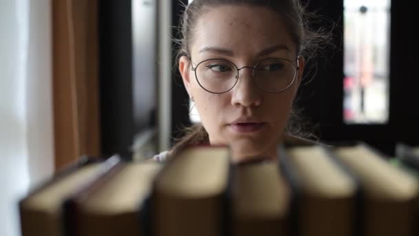 Chica estudiante elige un libro y lo toma de la estantería — Vídeo de stock