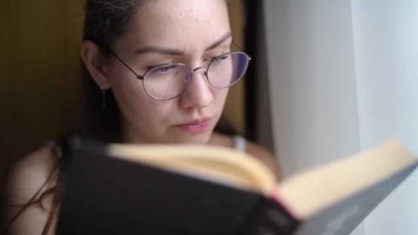 Joven mujer está leyendo un libro, vista desde detrás de un libro, primer plano — Vídeo de stock