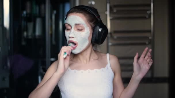 Egy Lány Gondoskodó Maszkkal Arcán Egy Fogkefébe Énekel Miközben Zenét — Stock videók