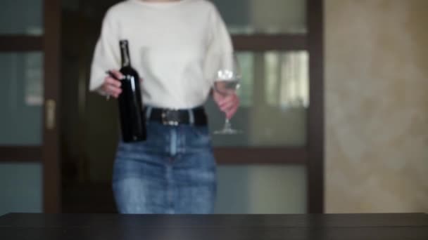 女の子はワインとガラスでキッチンに入りテーブルの上でワインを開け始めます — ストック動画